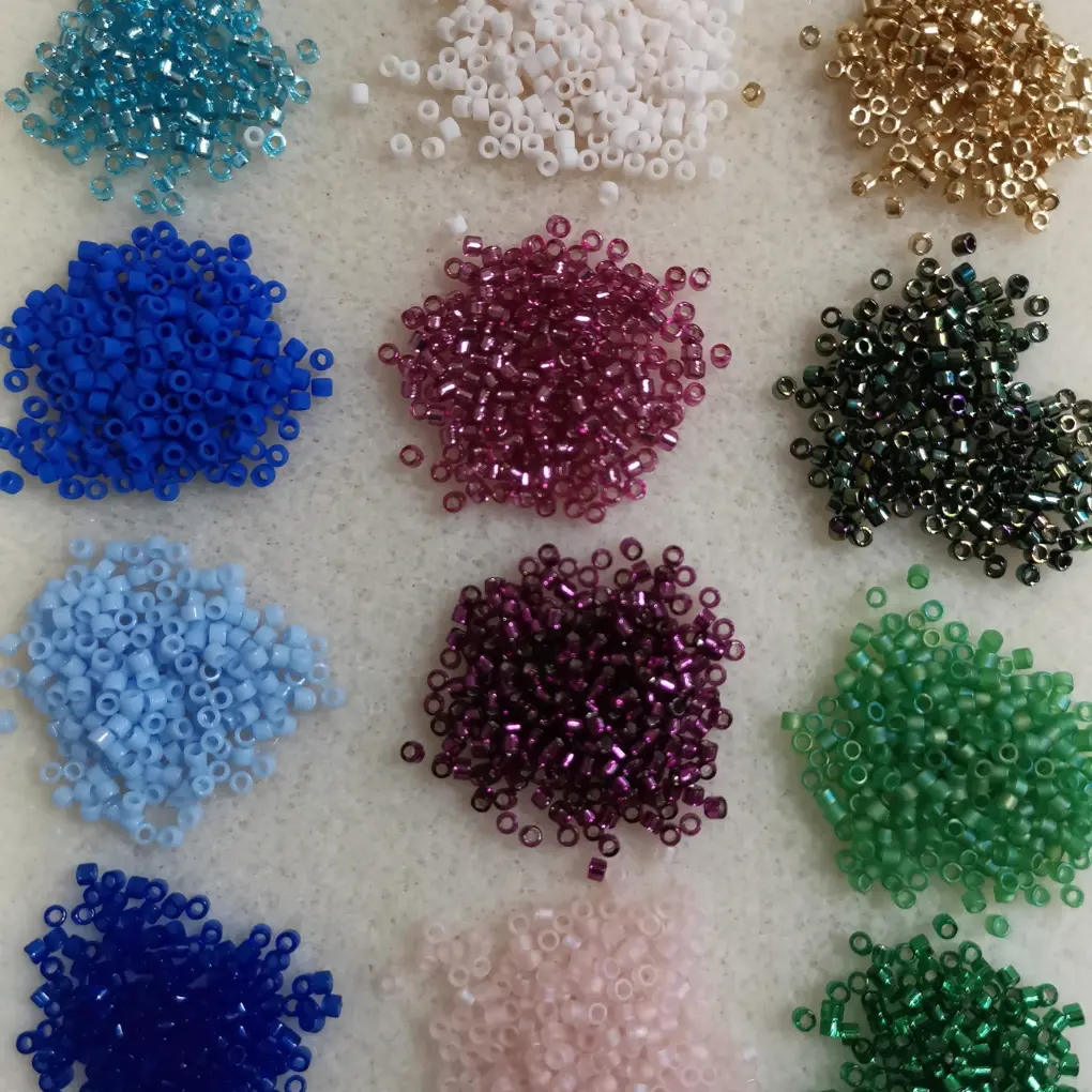 perles Miyuki en petits tas rangés par couleur sur un tapis