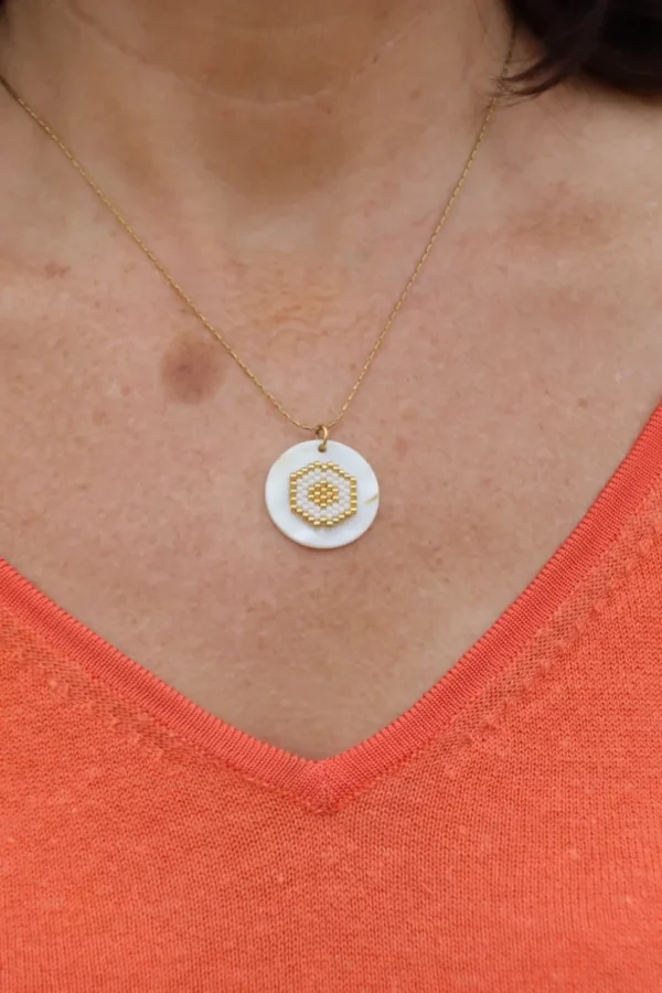 Collier avec tissage blanc et doré, collé sur un palet de nacre, porté sur peau, t-shirt en V orange.