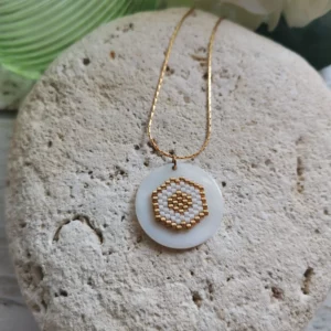 Collier tissage de perles Miyuki blanches et dorées, en forme de nid d'abeilles, collé sur palet de nacre rond . Monté sur chaine en acier inoxydable, il est posé sur une pierre blanche.