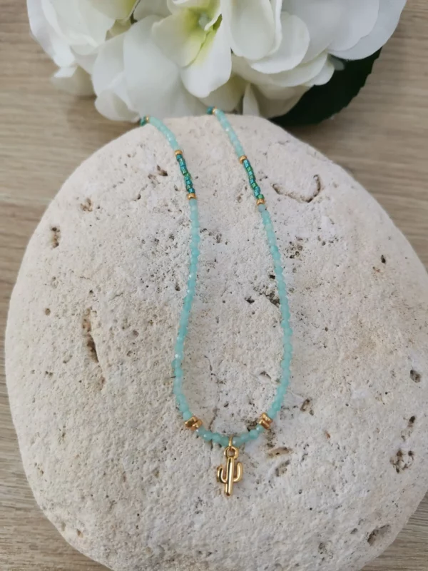 Collier en perles naturelles d'Amazonite de 3mm, associées à des perles Miyuki bleues vertes et un petit cactus doré. IL est posé sur une pierre blanche.