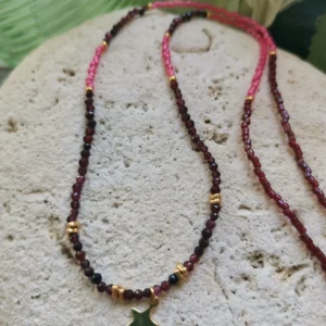 Collier de perles naturelles de Grenat et perles Miyuki fuchsia, orné d'une étoile dorée. Le tout posé sur une pierre blanche.