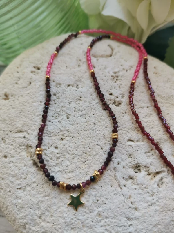 Collier de perles naturelles de Grenat et perles Miyuki fuchsia, orné d'une étoile dorée. Le tout posé sur une pierre blanche.