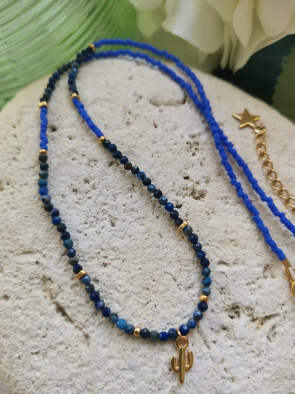 Collier de perles facettées de Lapis lazuli de 3mm, associées à des perles Miyuki bleu cyan. Un petit pendentif cactus rehausse le collier qui est posé sur une pierre blanche.