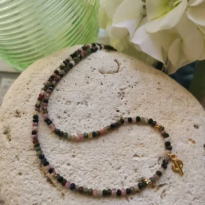 Collier de perles facettées de Tourmaline de 3mm, orné d'un petit cactus doré. Le tout posé sur une pierre blanche.