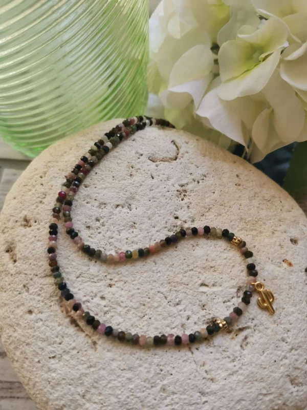 Collier de perles facettées de Tourmaline de 3mm, orné d'un petit cactus doré. Le tout posé sur une pierre blanche.