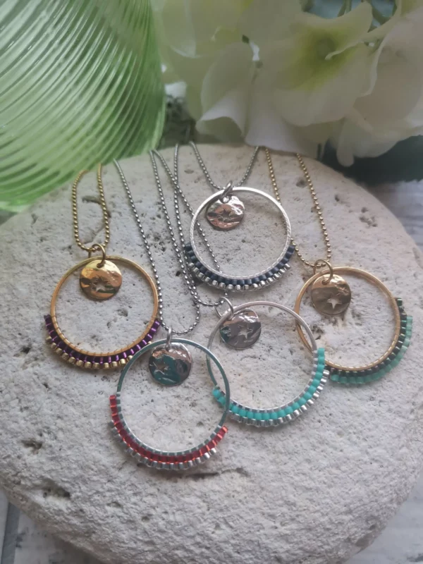 Ensemble de colliers avec un anneau tissé à moité de perles Miyuki et orné d'une breloque ronde ajouré d'une étoile. Le tout posé sur une pierre blanche.